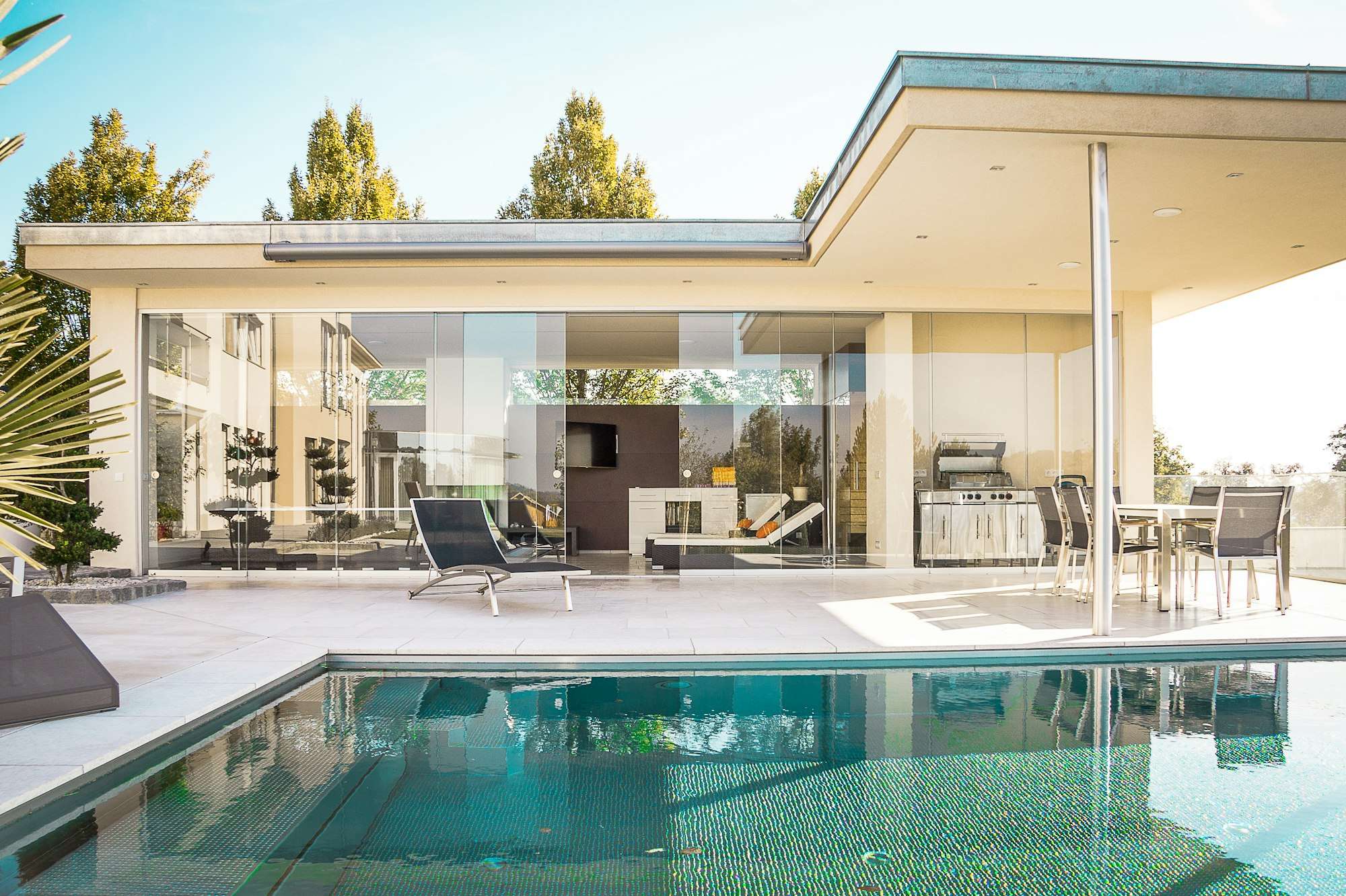 Piscine rénovée devant une villa d’architecte avec baies vitrées et terrasse couverte