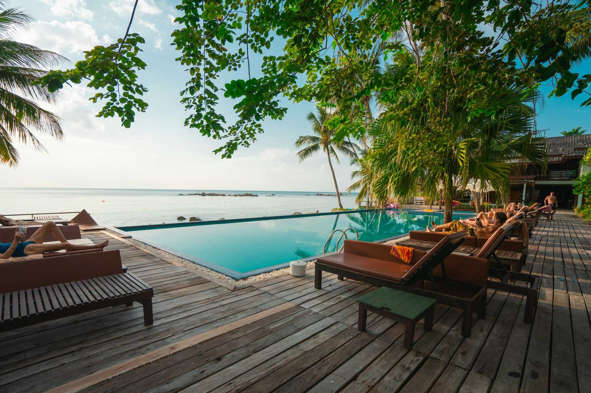 Piscine à débordement face à la mer, bordée d’une terrasse en bois et de transats