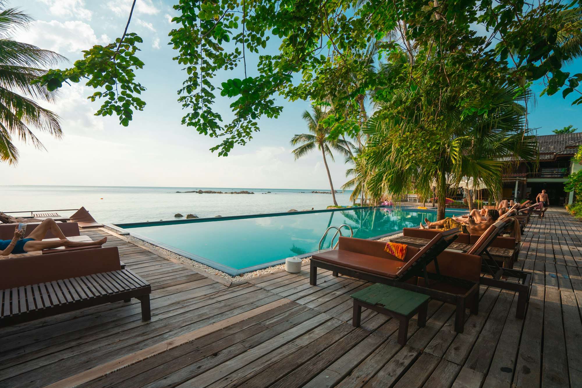 Piscine à débordement face à la mer, bordée d’une terrasse en bois et de transats